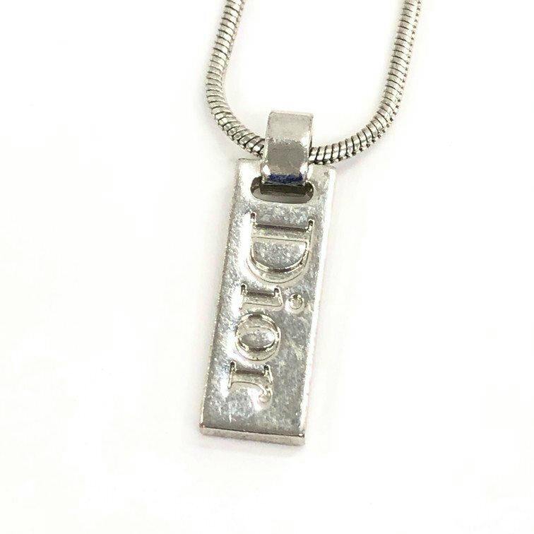 Close-up of a rectangular metal Christian Dior necklace pendant with a raised "DIOR" logo on a snake chain.