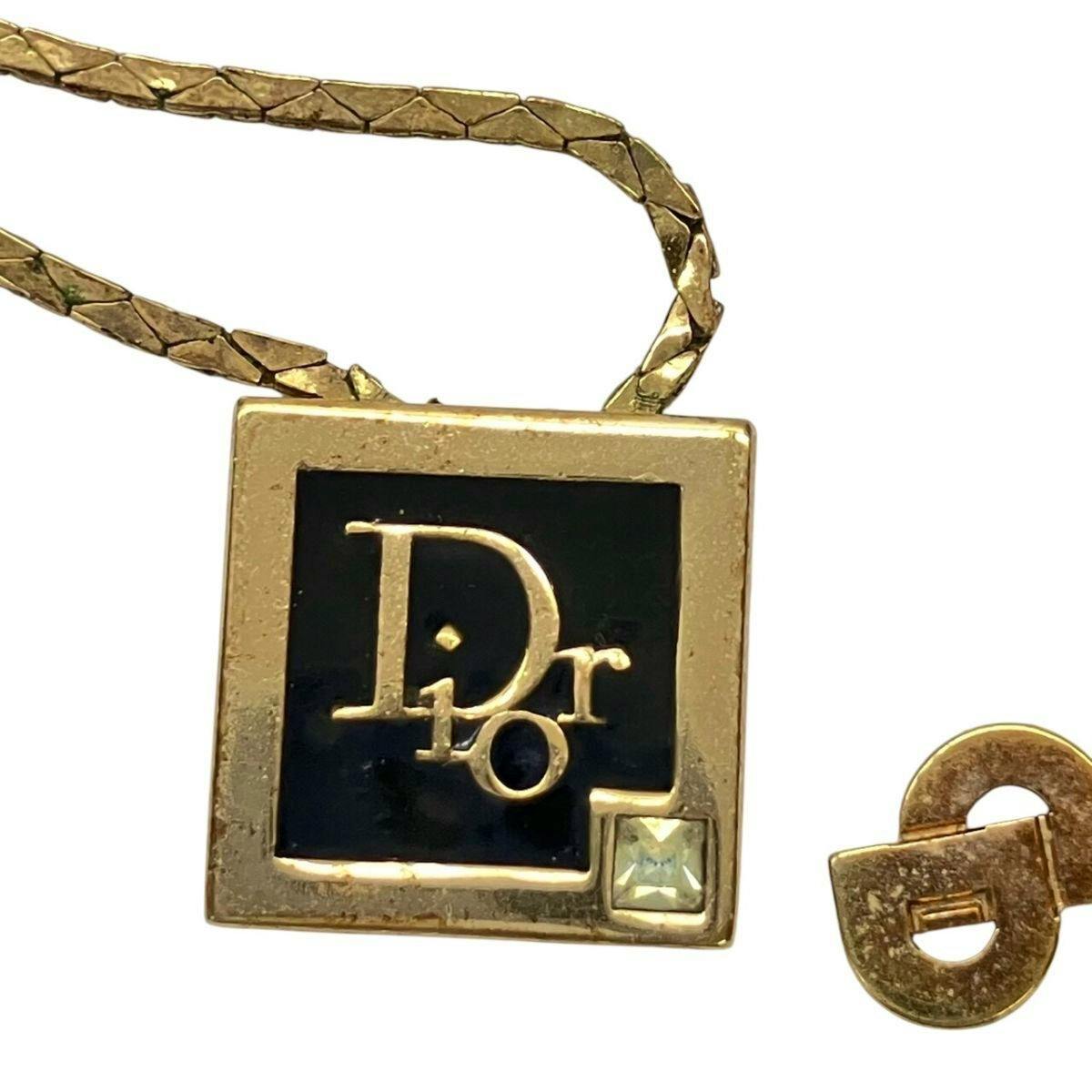Close-up of the gold-color Christian Dior square necklace pendant with black inset, Dior logo plate and a small stone on its gold chain.