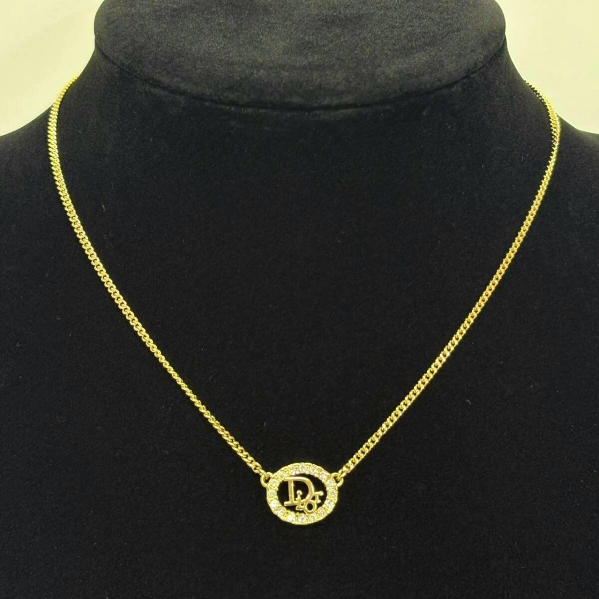 Gold-color Christian Dior necklace with a round rhinestone logo pendant displayed on a black bust.
