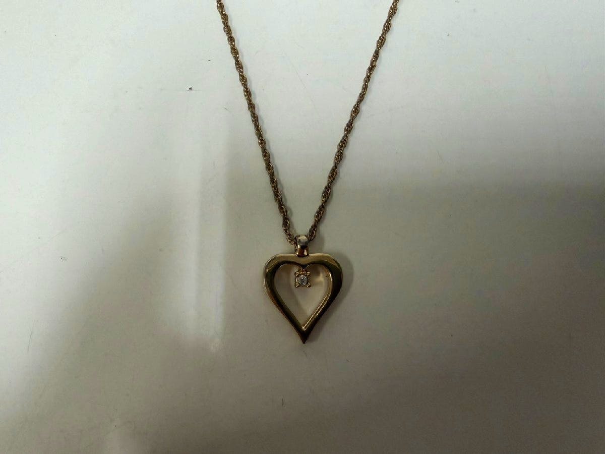 Christian Dior heart necklace with a hollow heart pendant and a small rhinestone charm suspended inside on a twisted chain against a white background.