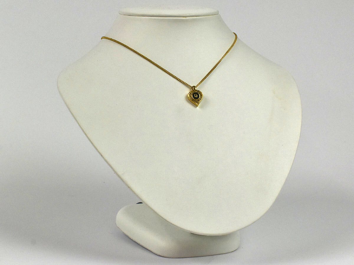 Gold-tone Christian Dior necklace with a heart-shaped pendant featuring a black logo center and surrounding rhinestones displayed on a white bust.