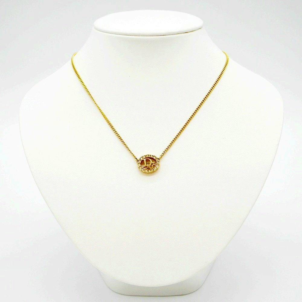 Gold-colored Christian Dior logo necklace with rhinestones shown on a white display bust.