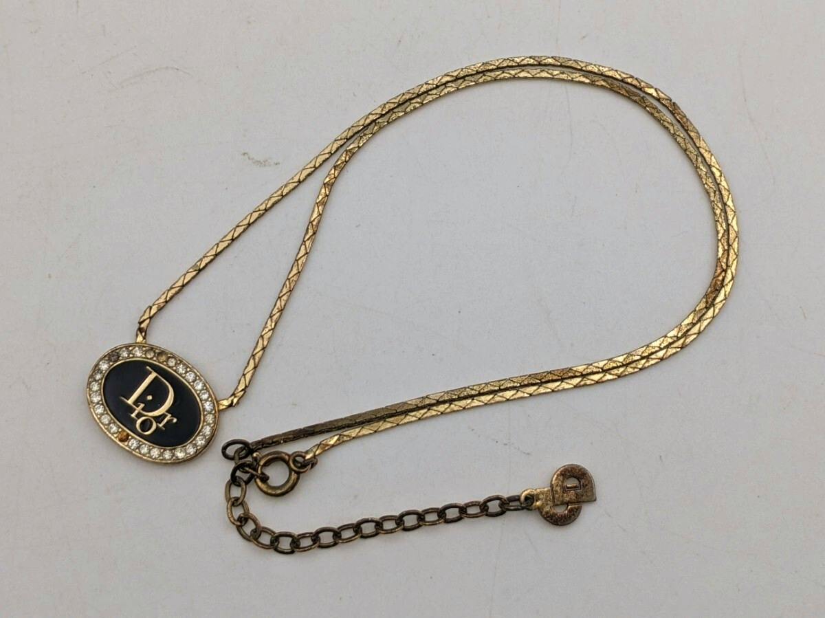 Gold-tone Christian Dior necklace laid flat showing an oval logo pendant with surrounding stones and its adjustable chain on a white background.