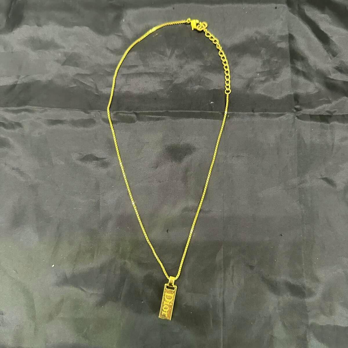 Gold-colored Christian Dior logo pendant necklace laid flat on a black fabric background.