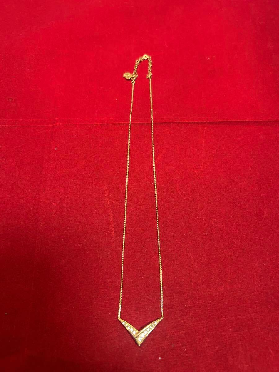 Full Christian Dior necklace with a V-shaped crystal pendant and chain laid on a red background.