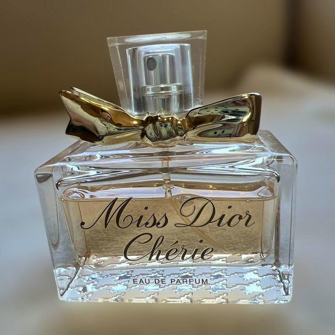 Close-up of the Miss Dior Chérie eau de parfum bottle showing the front label, liquid inside, and a decorative gold bow.