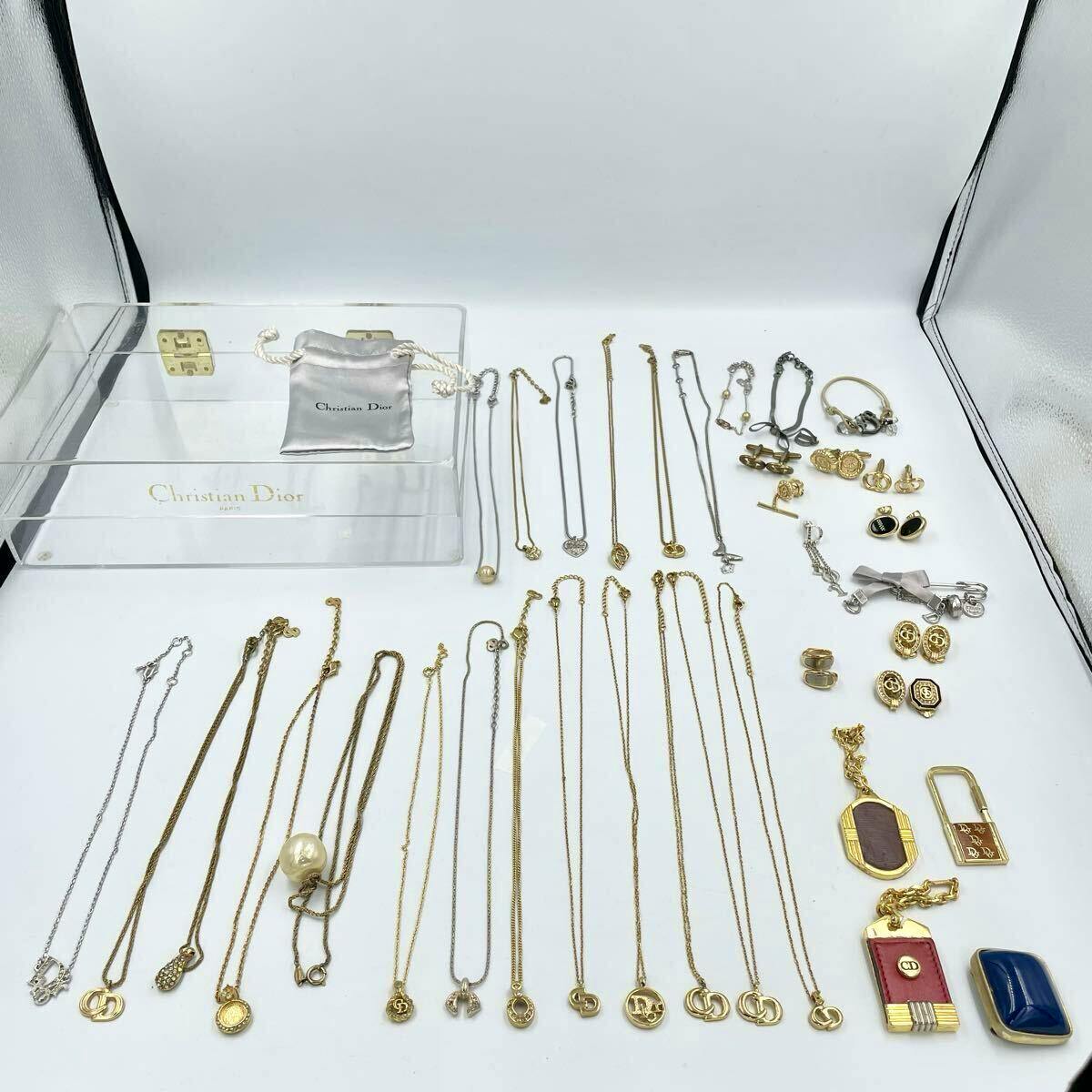 A large assortment of Christian Dior necklaces, bracelets, earrings, and charms laid out on a white background with a clear Christian Dior display box and pouch.