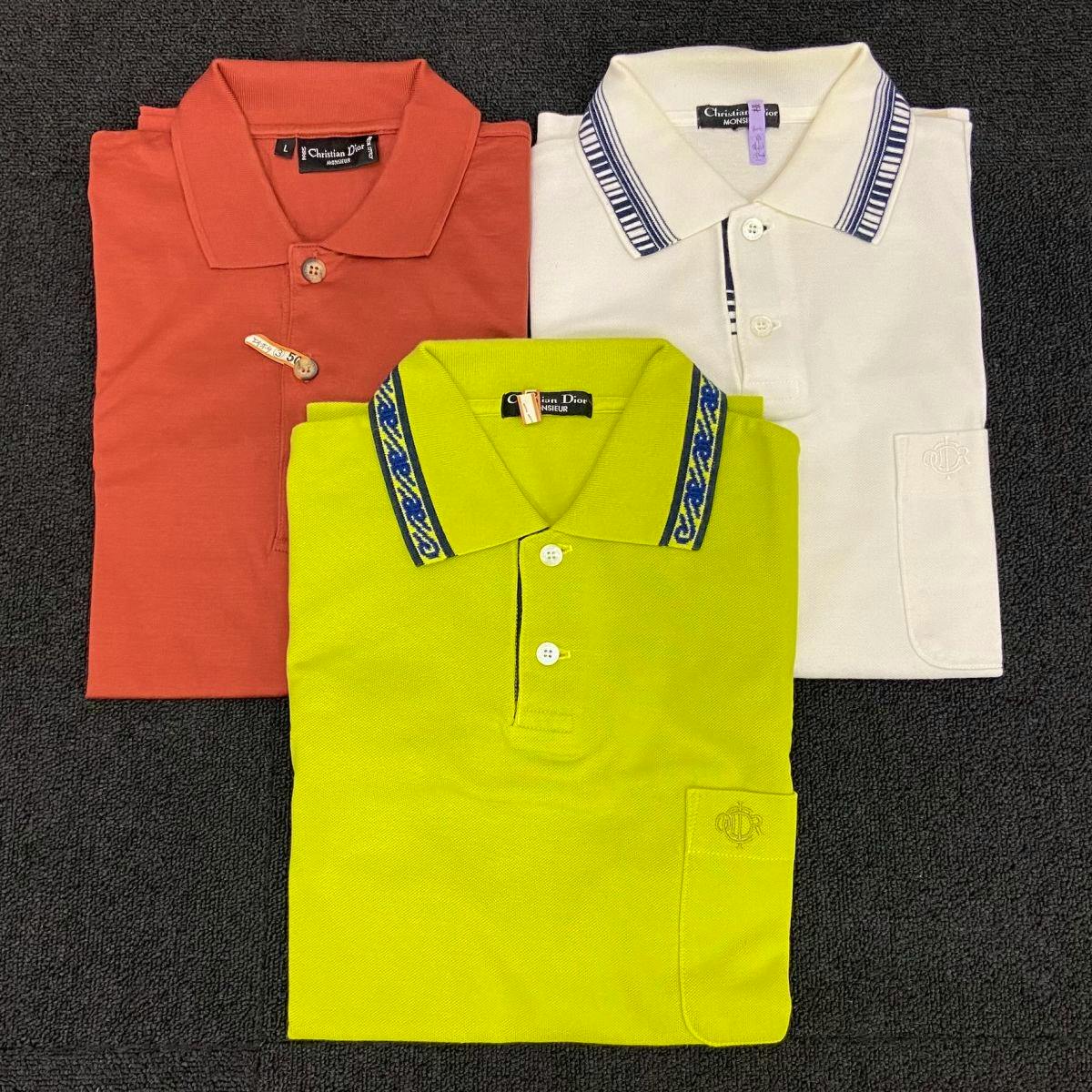 Three folded Christian Dior MONSIEUR polo shirts (red, white, and bright green) arranged on a dark textured surface.