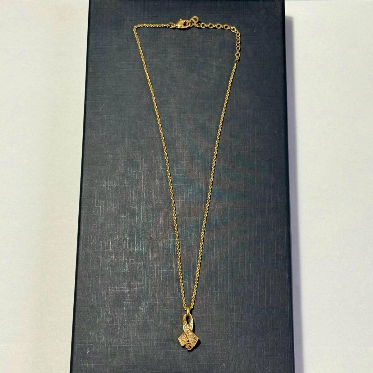 A gold-colored Christian Dior necklace with a small ribbon-shaped pendant displayed on a dark textured surface.