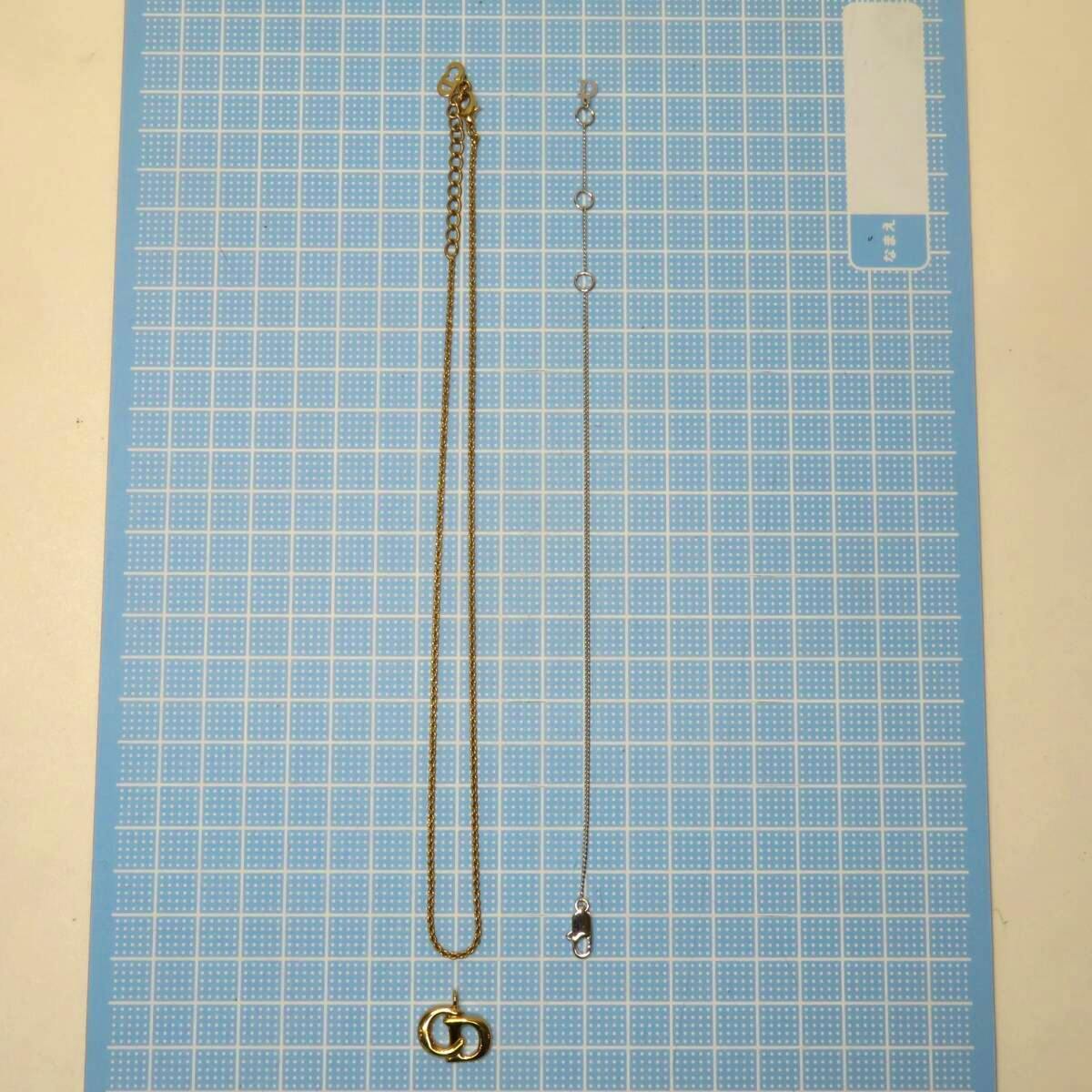 Two pieces from the set laid flat on a blue grid background: a gold chain with an interlocking pendant and a thin silver chain with a lobster clasp.