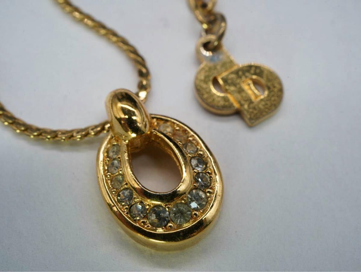 Close-up of the gold-tone Christian Dior necklace pendant with clear stones, chain, and clasp tag visible.