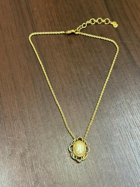 Gold-tone Christian Dior necklace (non-precious metal) with a decorative pendant featuring an oval light-colored center, laid flat on a brown wooden surface.