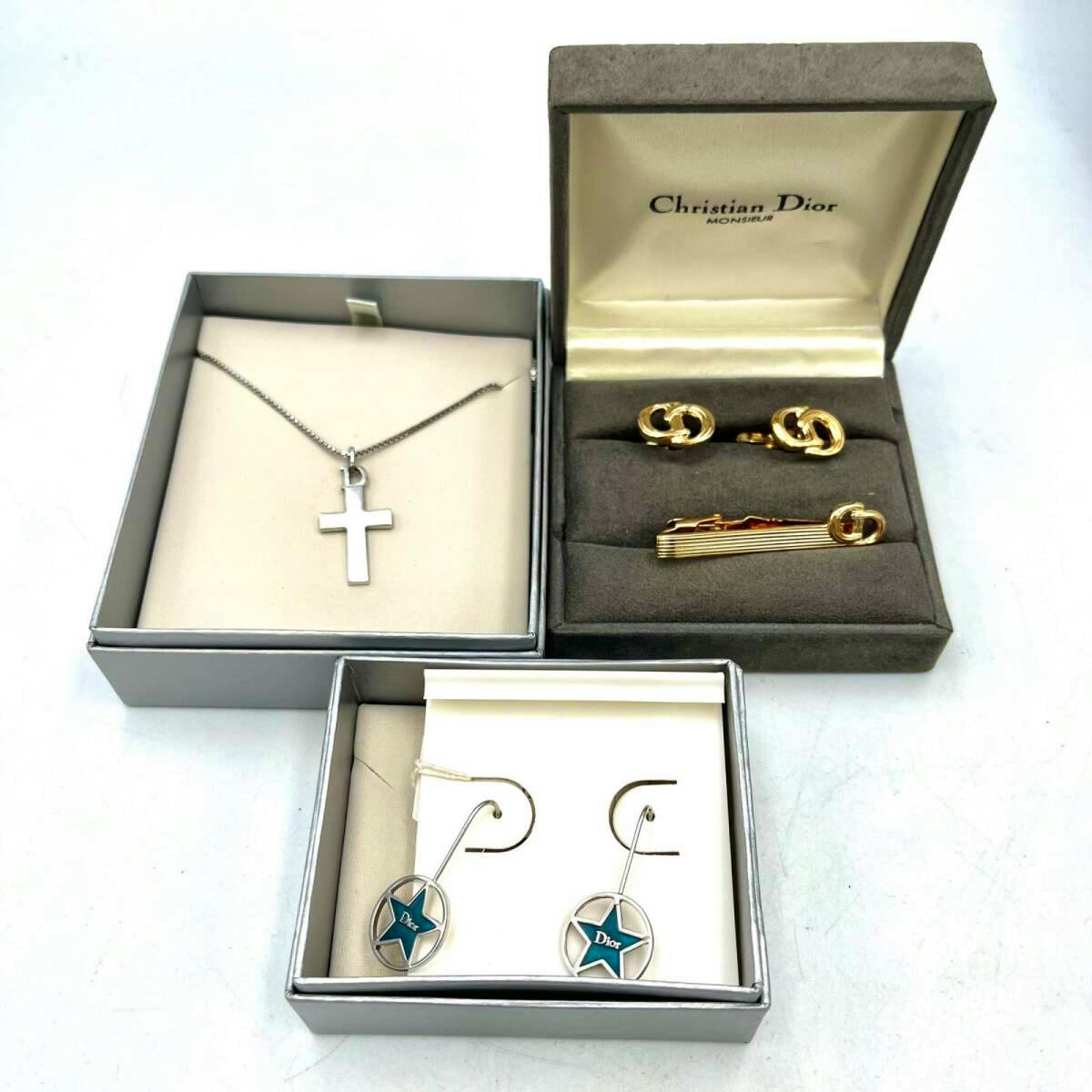 Top-down photo of a Christian Dior set showing a cross necklace, a pair of star-design earrings, and gold cufflinks with a tie clip in display boxes.