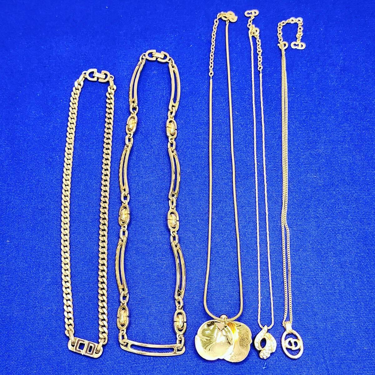 Five gold-tone Christian Dior necklaces arranged on blue fabric, showing various chains and pendants.