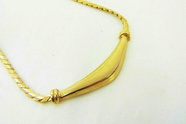Close-up photo of a gold-tone necklace chain with a curved bar pendant on a white background.