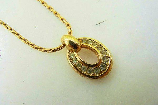 Close-up of a gold-tone necklace pendant with small clear stones on a chain.