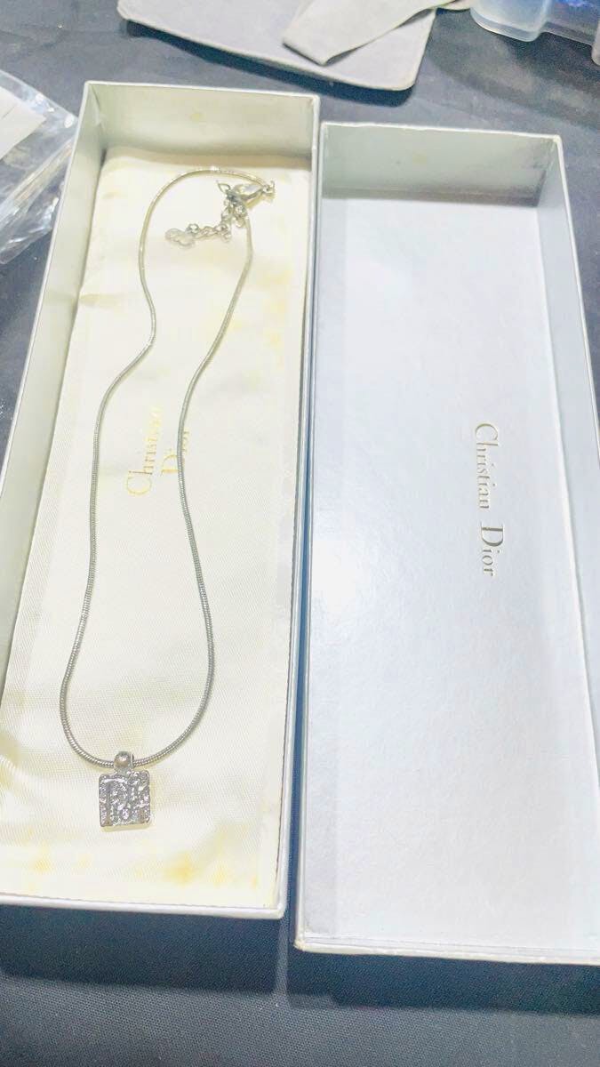 A Christian Dior necklace with a square textured pendant displayed inside its Christian Dior box.