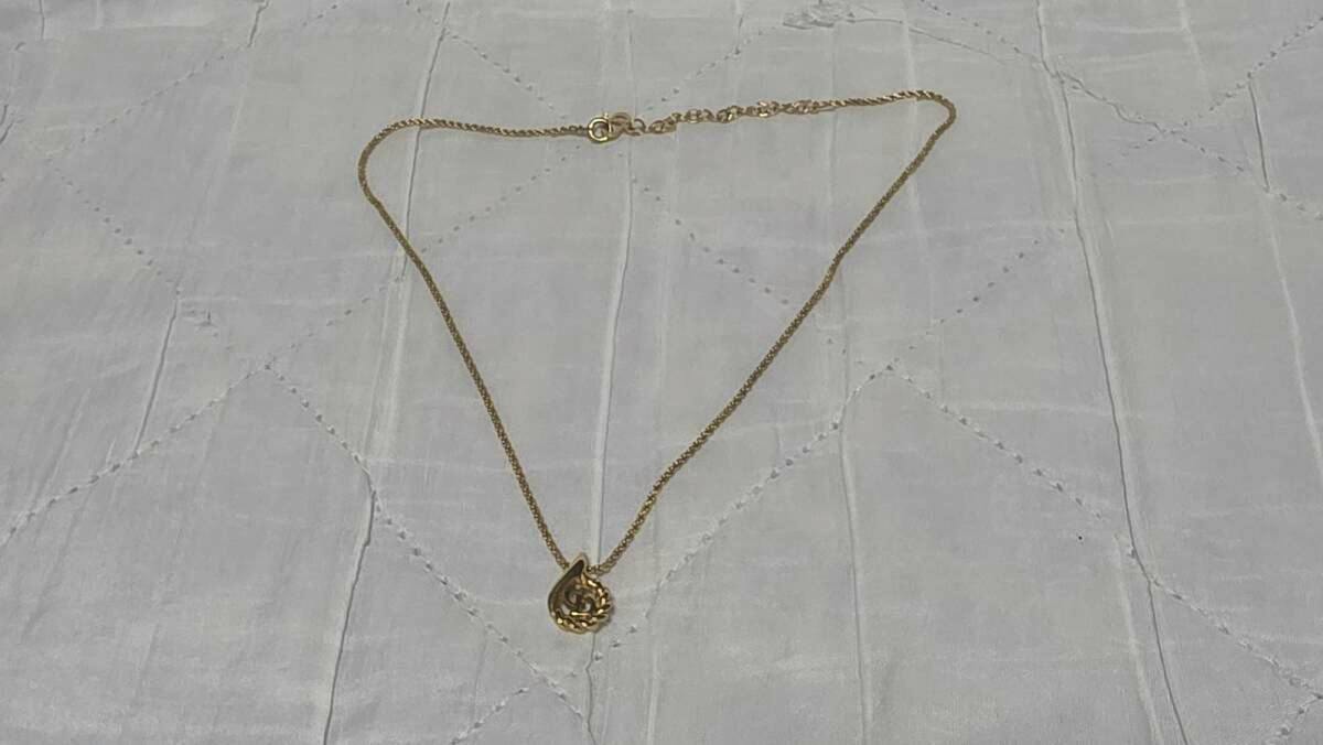 Photograph of the Christian Dior necklace laid flat, showing its chain, clasp, and a teardrop pendant with a CD logo.