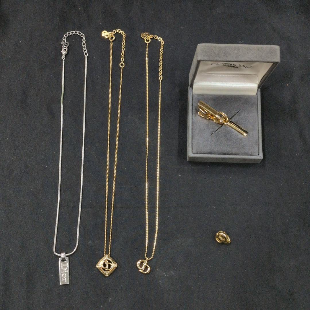 Several Christian Dior necklaces, a tie clip in its box, and a single earring displayed on a black background.