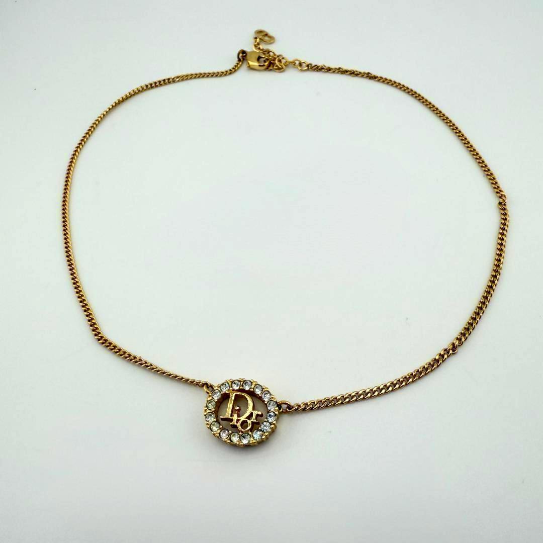 Gold-tone Christian Dior necklace with a round crystal-studded pendant featuring the Dior logo on a white background.