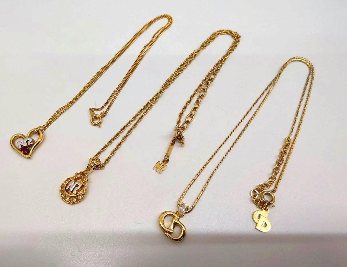 Several gold-tone logo necklaces laid flat on a white background, including a Christian Dior "CD" charm and Nina Ricci "NR" pendants.