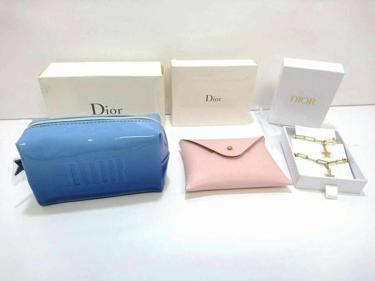 Blue Dior pouch with embossed DIOR, a pink card holder, and a gold-tone charm chain displayed with Dior boxes.