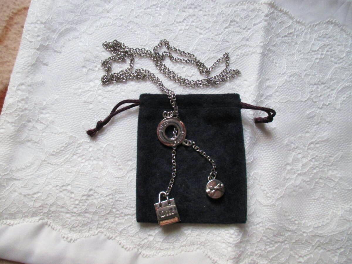 Silver-tone Christian Dior novelty necklace with chain, round ring connector, small round charm, and padlock charm displayed on a black drawstring pouch over white lace.