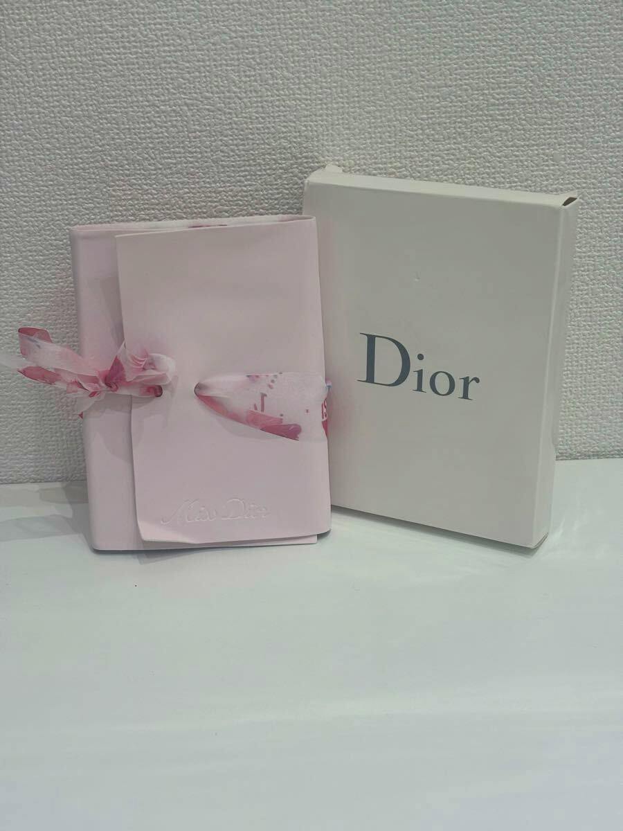 Pink Christian Dior notebook tied with a floral ribbon displayed next to its white Dior box on a white surface.