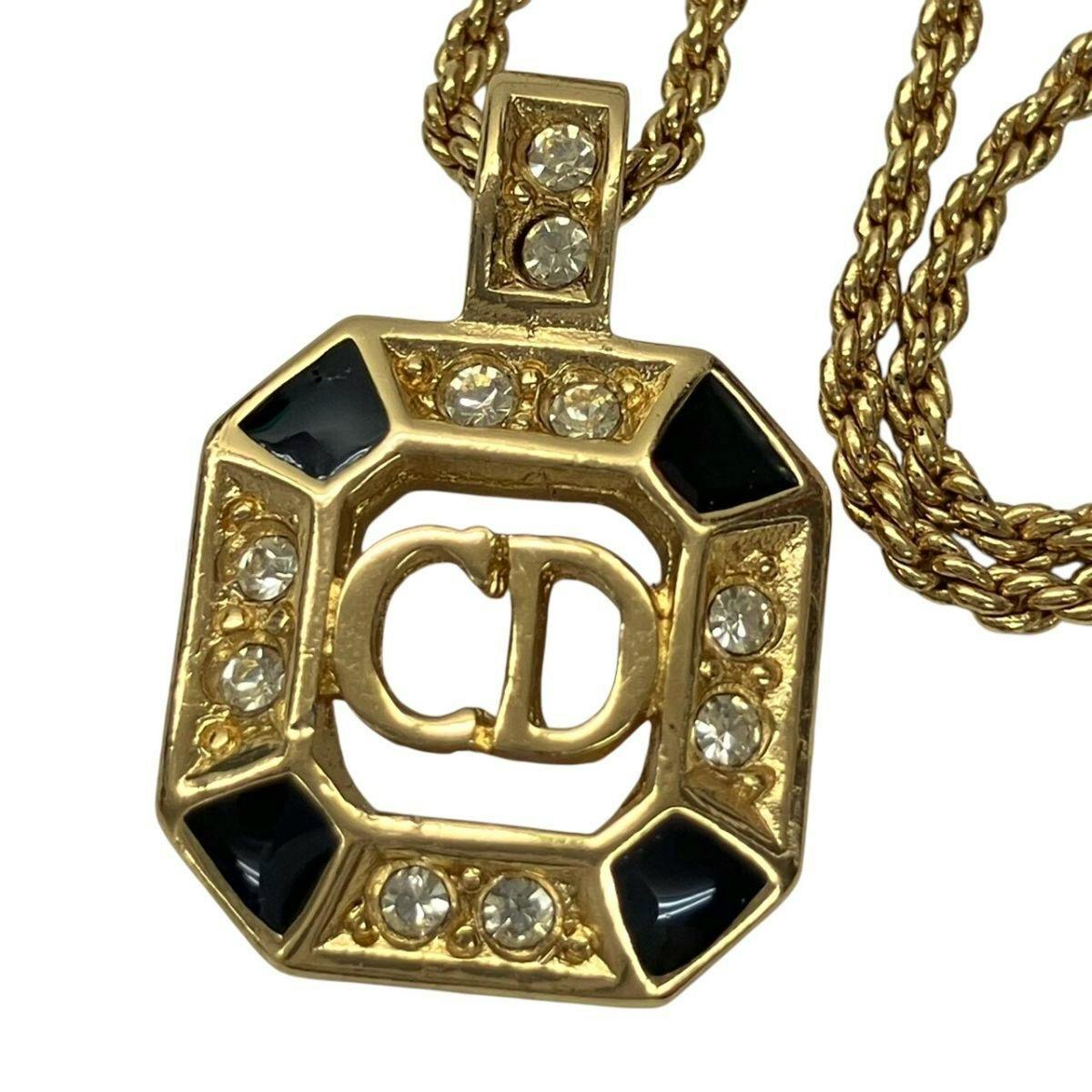 Close-up of the gold-color Christian Dior octagon pendant necklace showing the CD logo, black enamel corners, and rhinestone details on a twisted chain.