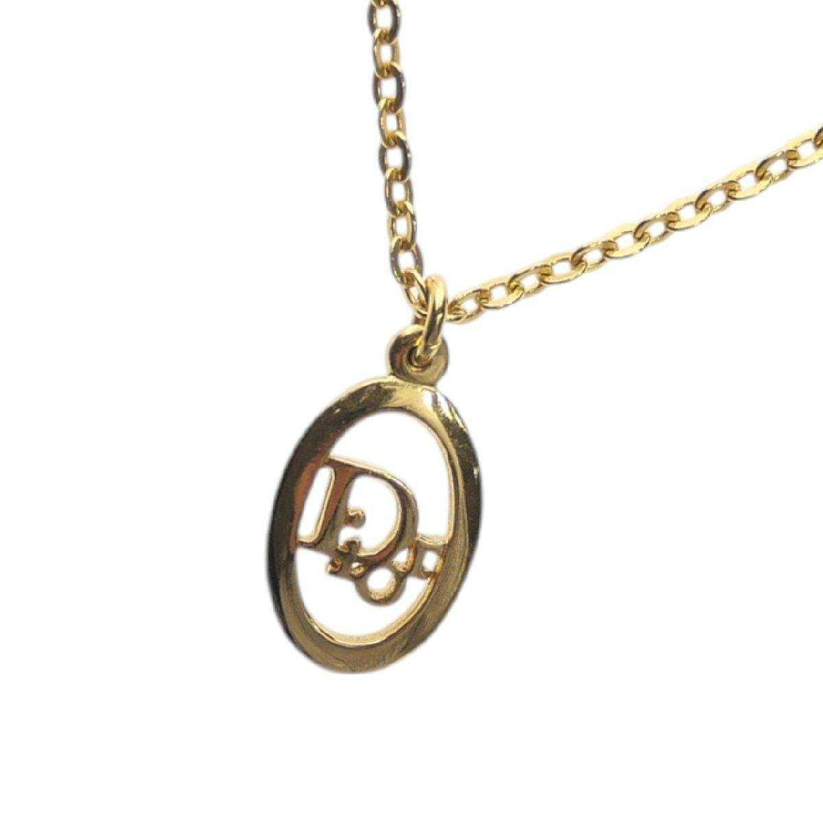 Close-up of the gold-colored Christian Dior oval pendant featuring a CD logo on a chain.