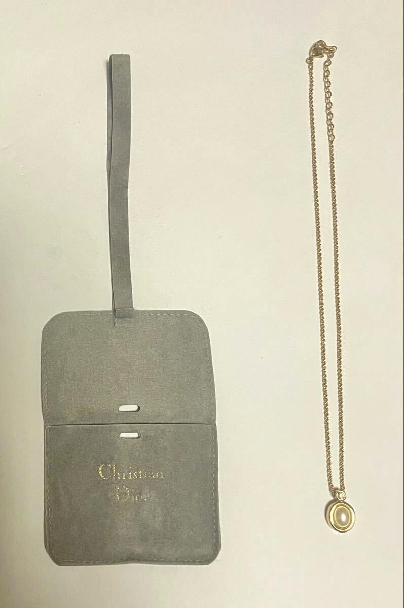Christian Dior necklace with an oval pendant on a chain displayed beside a gray Christian Dior pouch.