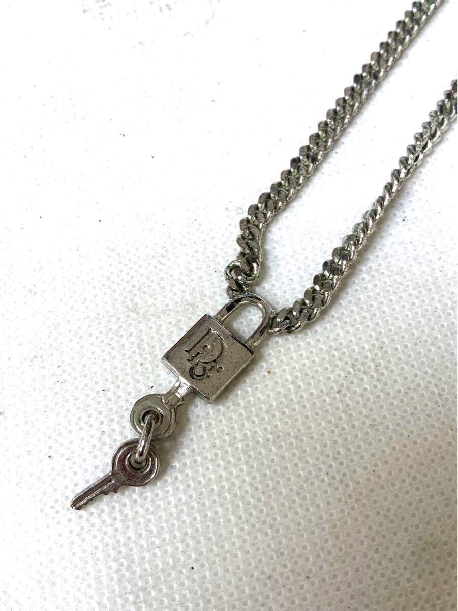 Close-up of a Christian Dior silver-tone necklace showing a padlock-style pendant with a small key on a white background.
