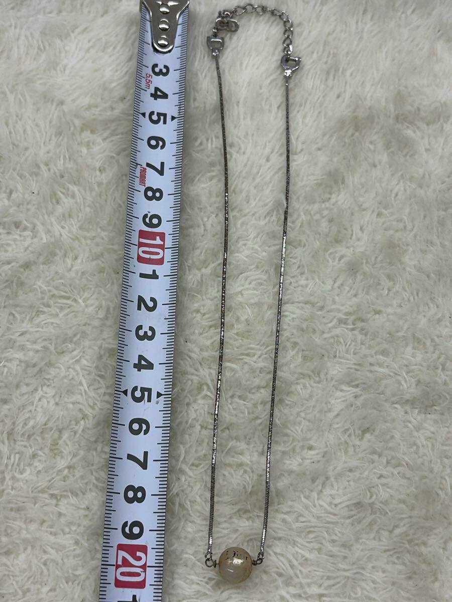 A Christian Dior pearl necklace with a single round pearl pendant and silver chain laid beside a measuring tape on a cream rug.