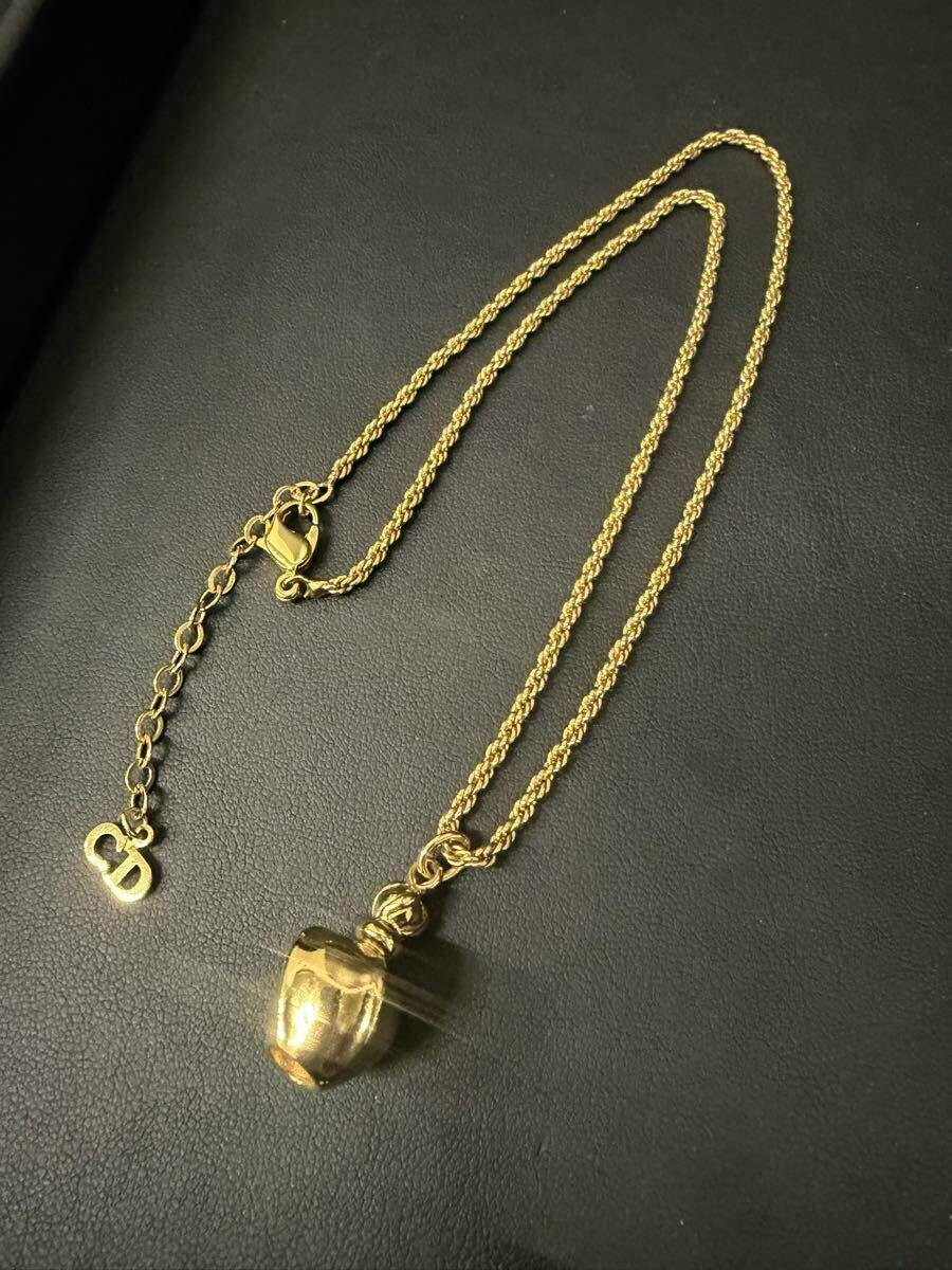 Gold-tone Christian Dior necklace with a perfume-bottle-shaped pendant displayed on a black surface.