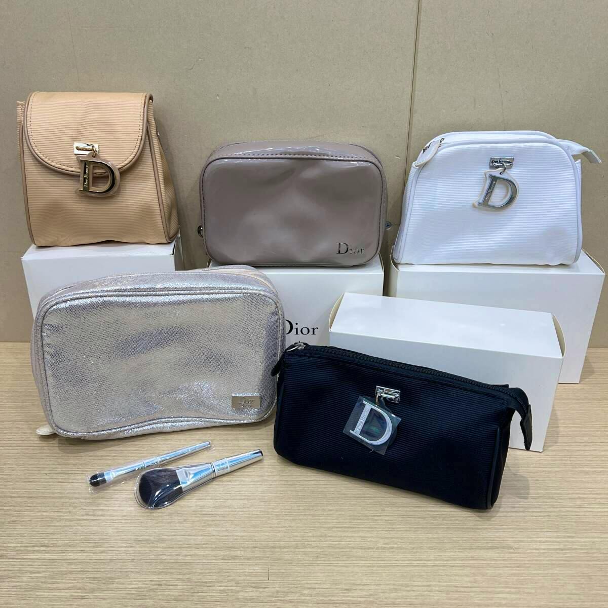 Five Christian Dior pouches in different colors arranged on boxes with two makeup brushes displayed in front.
