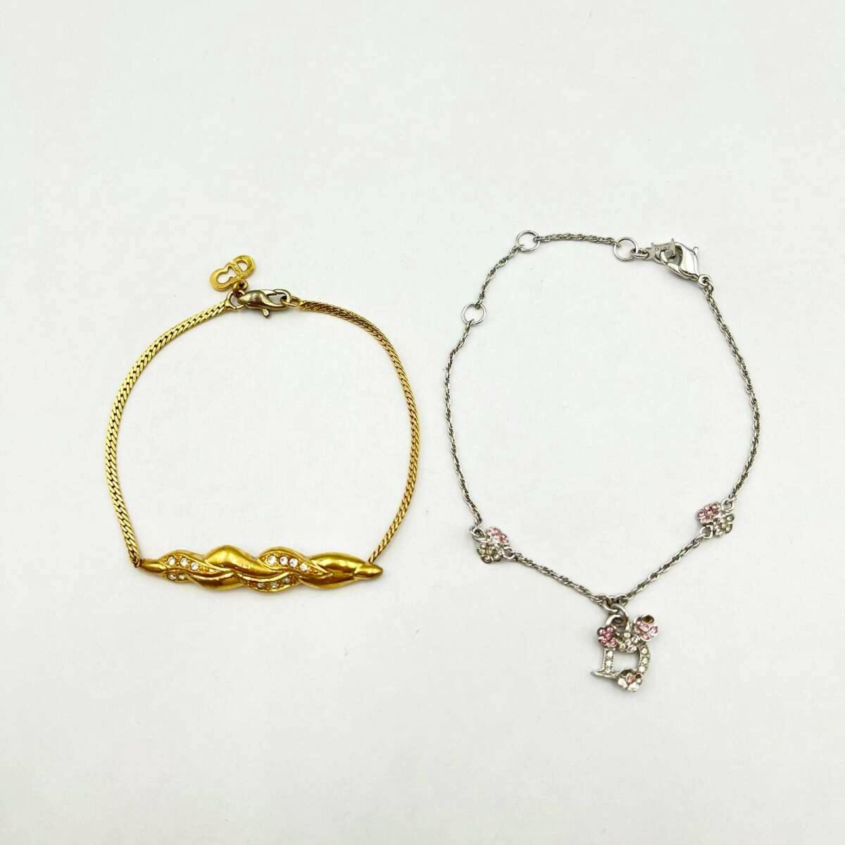 Two bracelets laid flat on a white background, one gold-tone and one silver-tone with pink rhinestones and a D charm.
