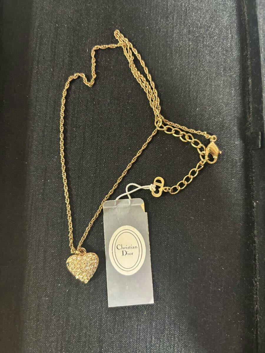Gold-tone Christian Dior heart pendant necklace with multiple small stones and an attached brand tag laid on a black surface.