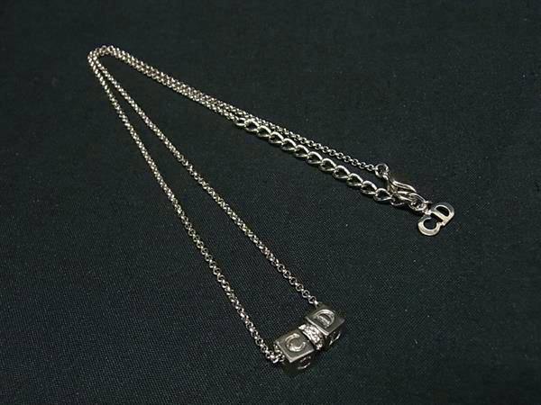 Silver-tone Christian Dior necklace with cube 'C' and 'D' letter pendant and a rhinestone spacer laid on black fabric.