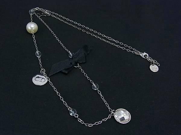 Silver-tone Christian Dior long necklace laid on a black background, showing a black ribbon, a faceted round pendant, clear bead accents, a pearl-like bead, and a small CD charm.