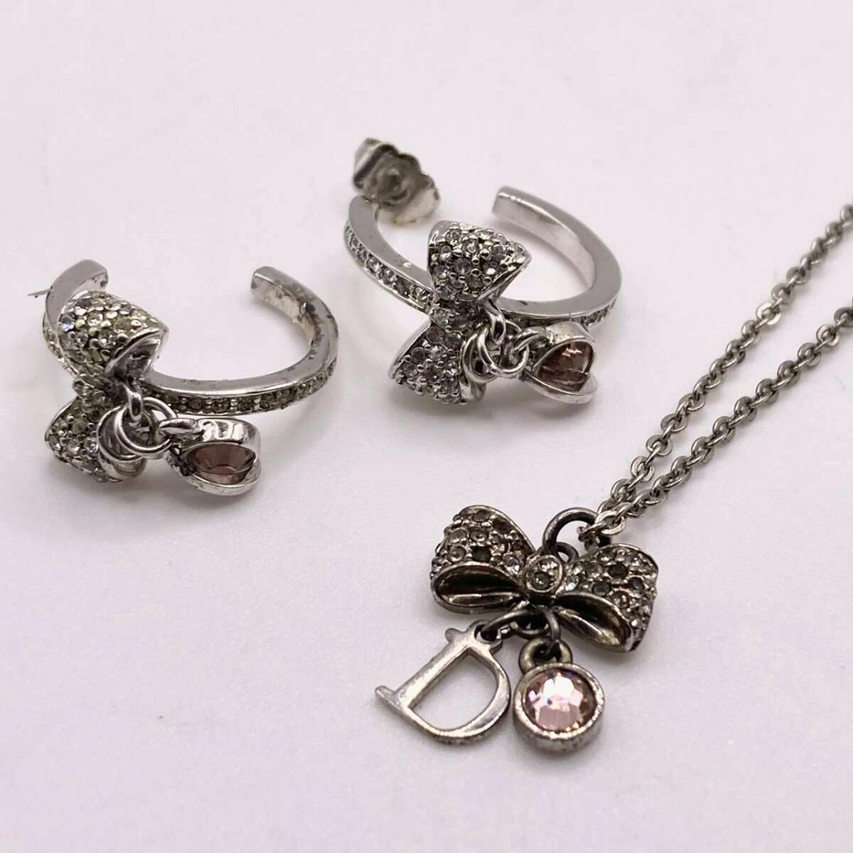 Two silver-tone bow hoop earrings and a matching pendant necklace with a 'D' charm and pink stone on a white background.