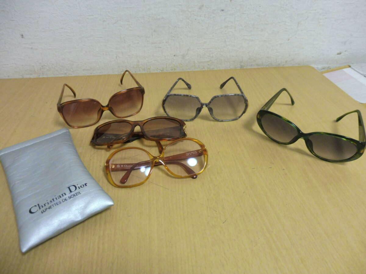 Five sunglasses and a Christian Dior pouch arranged on a wooden surface.