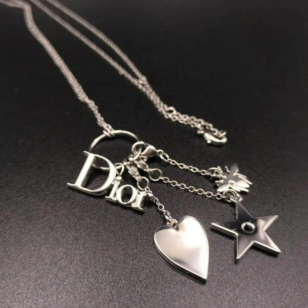 Close-up of a silver Christian Dior necklace showing the Dior letter charm with heart and star pendants on a black background.