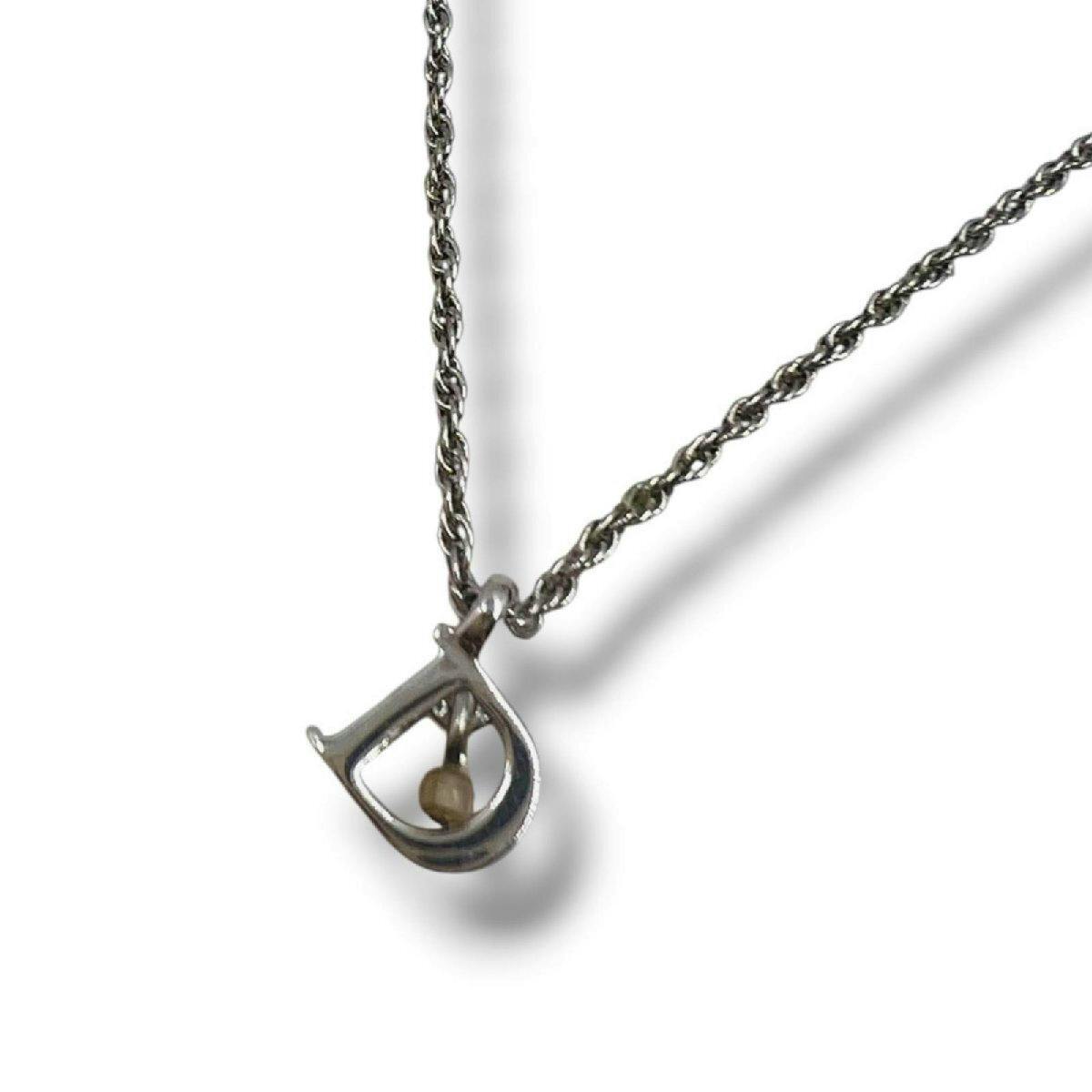 Silver Christian Dior necklace with a D-shaped pendant containing a small bead, shown on a twisted rope chain against a white background.