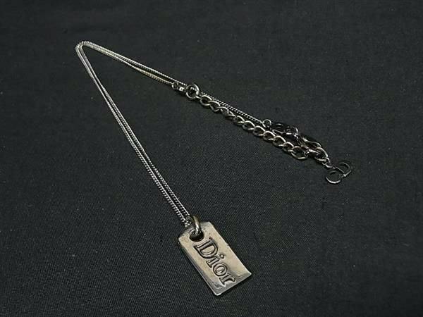 Silver-tone Christian Dior necklace with a rectangular "Dior" pendant laid on a black fabric background.