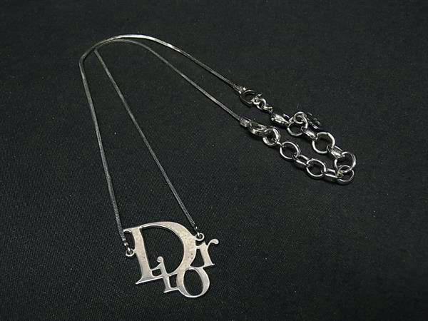 Silver-tone Christian Dior necklace with a Dior pendant and chain laid on a black background.