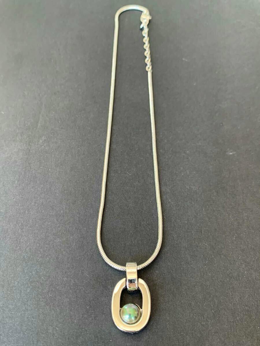 Silver-colored necklace with an oval pendant holding a round pearl, shown on a black background.