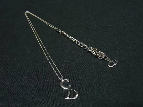 Silver-tone Christian Dior necklace with CD pendant and extension chain laid on a black background.