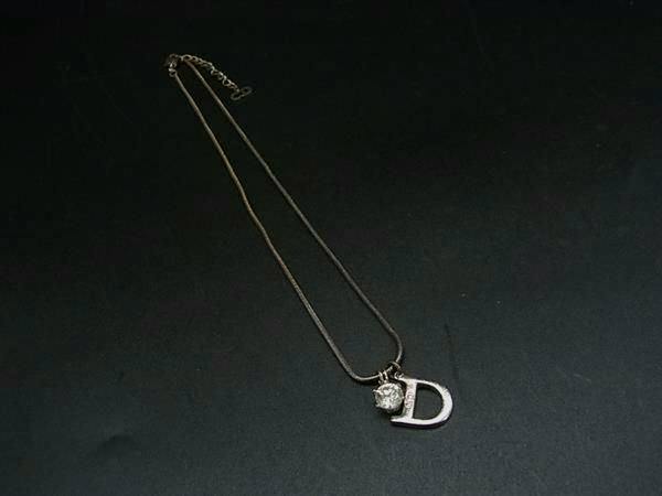 Christian Dior silver-toned necklace with a D-shaped pendant and a small round charm laid on a dark background.