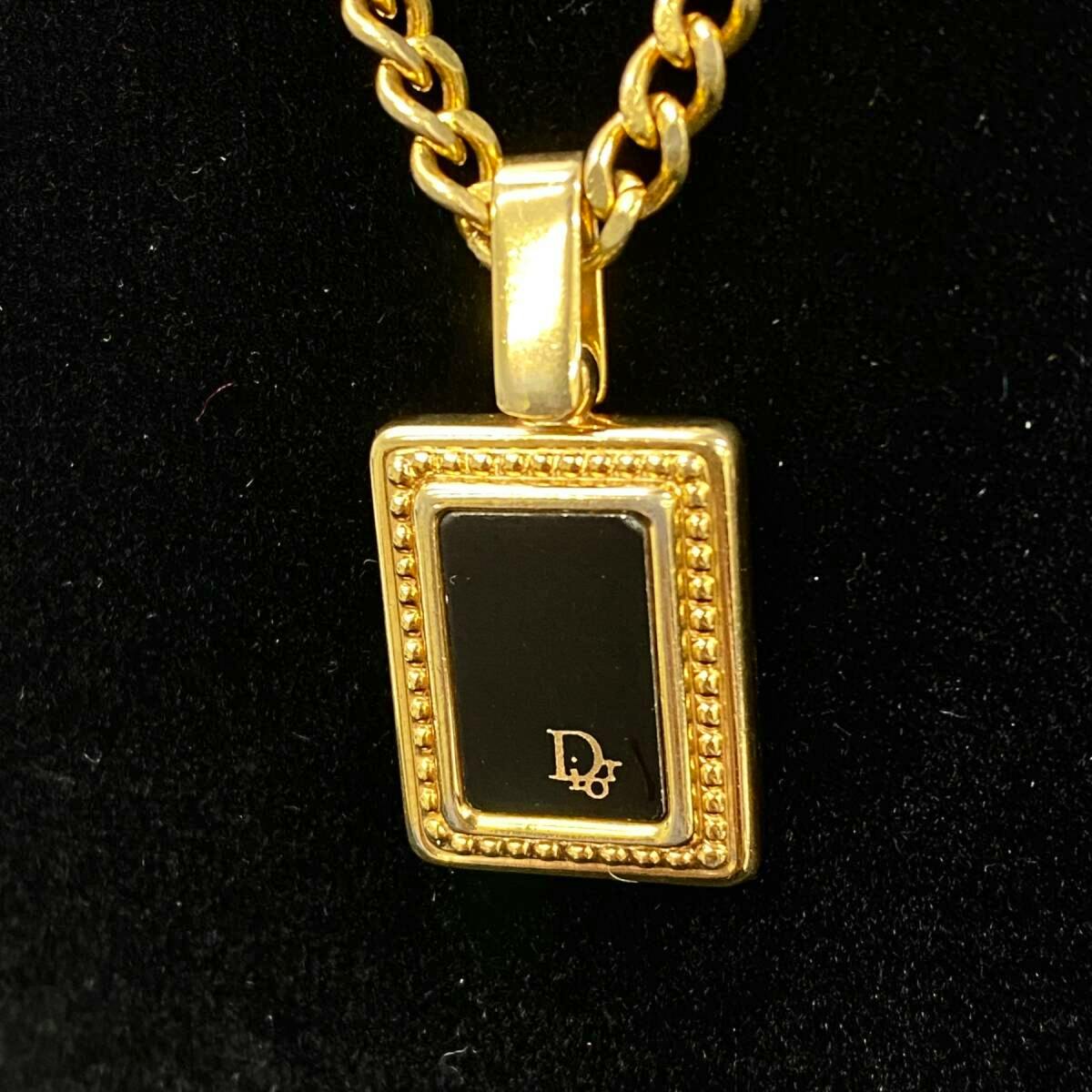 Close-up of a Christian Dior square logo plate pendant on a gold-tone chain against a black background.