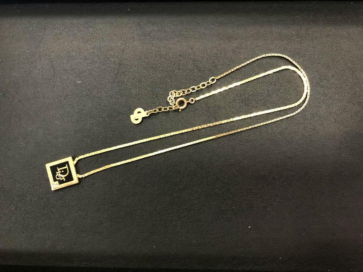 Gold-colored Christian Dior square pendant necklace laid flat on a dark background.